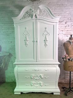 a white armoire sitting next to a mannequin on a stand in front of a brick wall