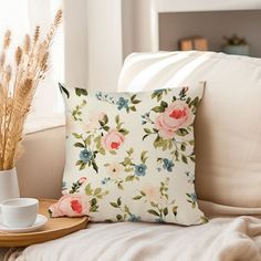 a flowered pillow sitting on top of a white couch next to a cup and saucer