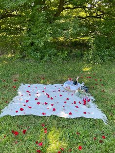 a woman laying on top of a white blanket covered in red flowers next to a tree