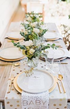 a baby shower table setting with white and gold place settings, greenery and napkins