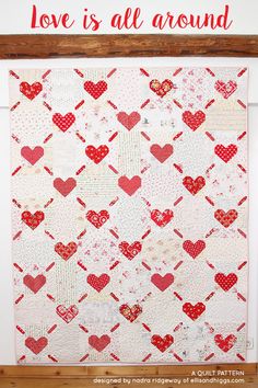 the love is all around quilt on display in front of a wooden frame with red and white hearts