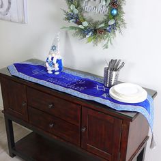 a wooden table topped with a blue and white christmas table runner next to a wreath