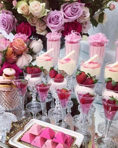 a table topped with lots of desserts and glasses filled with pink frosted treats