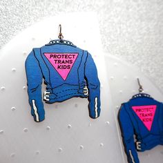 a pair of earrings with the words protect transs kids printed on them, hanging from hooks