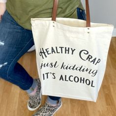 a woman holding a tote bag that says healthy crap just kidding it's alcohol