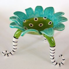 a green and white flower shaped object with black stripes on it's legs, sitting on a white surface