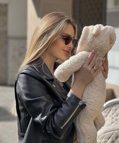 a woman holding a teddy bear in her hands while wearing sunglasses and a leather jacket