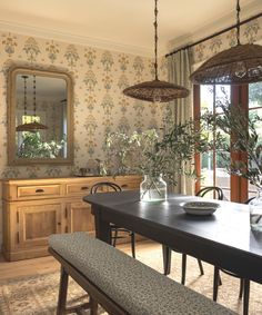 a dining room table and bench in front of a large window with floral wallpaper