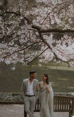 a man and woman standing next to each other on a bench in front of a tree