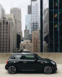 a small black car parked in front of tall buildings with skyscrapers in the background