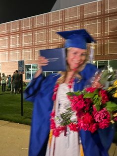 a woman in graduation cap and gown holding flowers on the side of a building at night