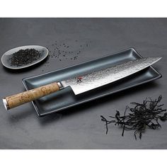 a large knife on a tray next to some black seeds and a spoon with a wooden handle