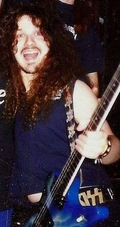 a man with long curly hair is holding a guitar and smiling at the camera while standing next to him