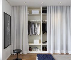 a white closet with clothes and shoes on it, next to a black footstool