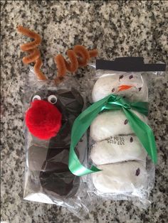 two frosted snowman cookies in plastic bags with green ribbon and reindeer nose on top