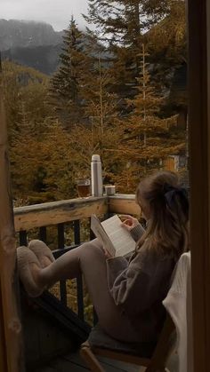 a woman sitting in a chair on top of a porch reading a book and holding a teddy bear