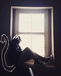 a person sitting on a window sill in front of a light coming through the window