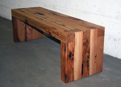 a bench made out of wood sitting on top of a cement floor next to a white brick wall