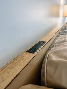 a remote control sitting on top of a wooden shelf next to a bed in a bedroom