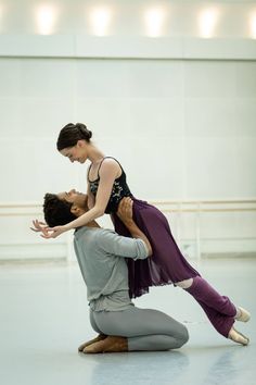 two ballerinas are performing on the floor in a dance studio, one is holding the dancer's leg