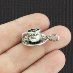 a small silver teacup charm on a persons hand