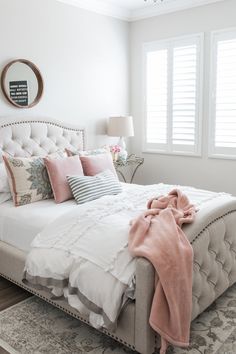 a white bed with pink and gray pillows