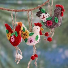 three handmade roosters hanging from a tree branch with red berries and green leaves