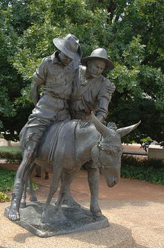 a statue of two men riding on the back of a cow in front of some trees