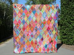 a colorful quilt sitting on the side of a road next to some bushes and trees