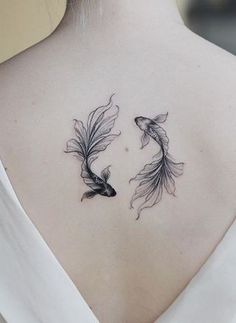 the back of a woman's neck with two goldfish tattoos on it