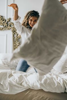 a woman in white shirt and jeans jumping on bed