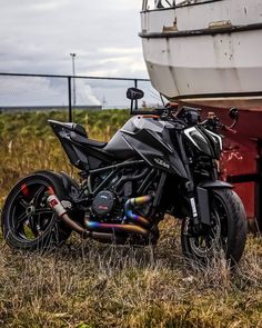 a motorcycle parked in front of a boat on dry grass next to a red trailer