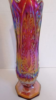 a colorful glass vase sitting on top of a wooden stand in front of a white wall