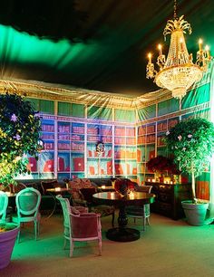 a room filled with lots of tables and chairs under a chandelier covered in green lights