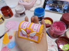 a person is holding a small box shaped like a heart with wings and hearts painted on it