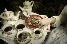 a table topped with cups and saucers filled with cookies next to teapots