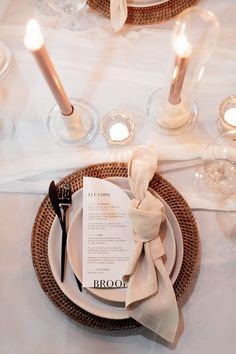 a place setting with napkins and silverware on a white table cloth, surrounded by candles