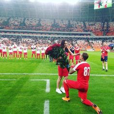 a man kneeling on top of a soccer field holding a bouquet of flowers next to another man