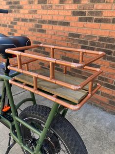 a green bike with a wooden seat and back rack on the front, parked in front of a brick wall