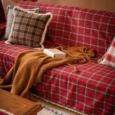 a red and black plaid couch with a blanket on it's back next to pillows