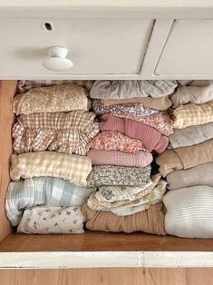 an open drawer filled with pillows and blankets on top of a wooden floor next to a white cabinet