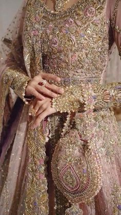 a woman wearing a gold and pink wedding dress with elaborate jewelry on her hands, standing in front of a white wall