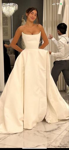 a woman standing in front of a mirror wearing a white dress and posing for the camera