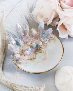 a white plate topped with crystals next to pink flowers and a vase filled with flowers