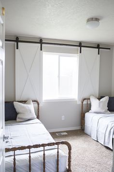 two twin sized beds in a bedroom with white walls and carpeted flooring next to windows