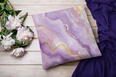 purple and gold marbled pillow sitting next to white flowers