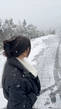 a woman standing on the side of a road covered in snow with her back to the camera