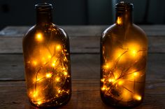 two glass bottles with lights in them sitting on a wooden table next to each other