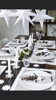 the table is set for christmas dinner with white stars hanging from the ceiling and candles