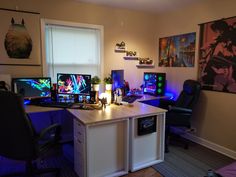 a desk with two computer monitors on it in front of a window and some pictures